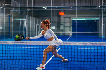 Female padel player playing a difficult forehand on the net