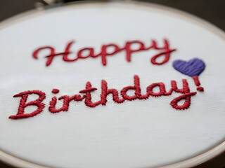 Embroidered "Happy Birthday" message with a purple heart on white fabric.