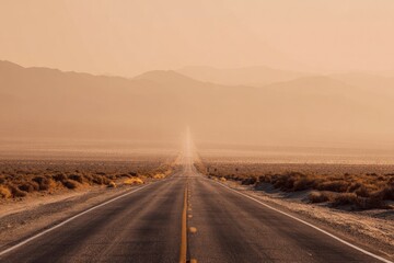 Fototapeta premium A long, straight road stretches into a hazy, golden desert landscape. Distant mountains are softly focused in the pale light