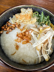 Traditional Indonesian chicken porridge or Bubur Ayam served with crackers, chili sauce, green sauce, and toppings on a wooden tray over rustic wooden table.