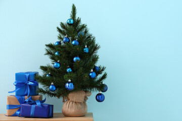 Beautiful Christmas tree with decorations and gifts on bench near blue wall in room