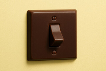 Chocolate colored light switch mounted on yellow wall adds warm and inviting touch to room. simple design complements various interior styles, enhancing overall aesthetic
