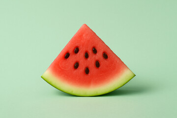 Fresh watermelon slice with vibrant red flesh and black seeds against soft green background, creating minimalistic and refreshing composition