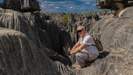A tired man with a backpack and safety gear sat down on a rock, resting. Cliffs with steep, furrowed slopes, sharp peaks against the blue sky. Madagascar. Tsingy De Bemaraha  