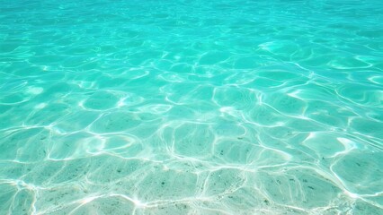 Obraz premium Clear turquoise water with sunlight reflections and sandy bottom