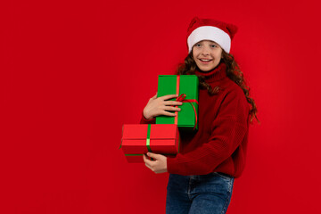 Smiling girl in Santa hat holds stacked Christmas gift boxes.