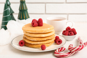 Plate of sweet pancakes with raspberries, candy canes, cup of tea and Christmas trees on white table