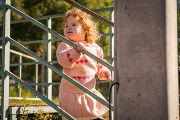 Young child exploring stairs at a park on a sunny afternoon in a cozy pink sweater
