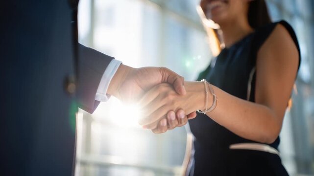 Slow panning shot capturing a close handshake between a man in a dark suit with shining sleeve cuff and a smiling woman wearing a bracelet in soft sunlight with blurred background