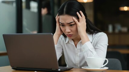 Young woman looking stressed while working on her laptop at a cafe - Powered by Adobe
