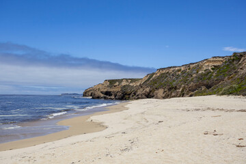Sandy beach with ocean waves and green cliffs under blue sky in California