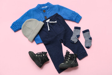 Stylish children's sweater, trousers, socks, hat and boots on pink background
