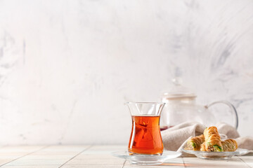 Glass of Turkish tea with teapot and tasty baklava on white tile table