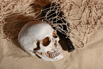 Human skull with bottle and net on sand