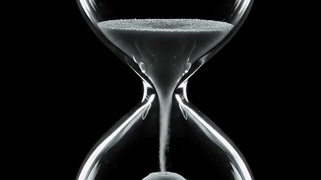 Close up of hourglass with sand falling against black background.