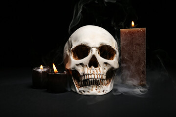 Human skull with burning candles and smoke on dark background