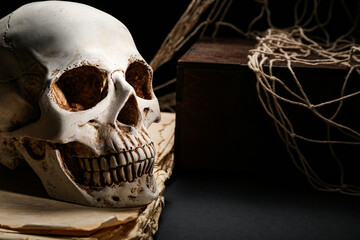 Human skull with old book, chest and net on dark table, closeup