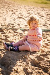Child playing in sandy area wearing warm sweater on a bright sunny day outdoors