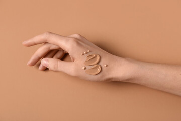 Female hand with samples of makeup foundation on brown background