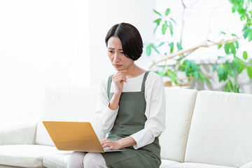 ソファに座りパソコンで仕事をするエプロンをつけた女性