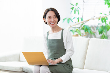 ソファに座りパソコンで仕事をするエプロンをつけた女性