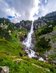 Dramatic mountain waterfall cascading down rocky slopes, lush greenery