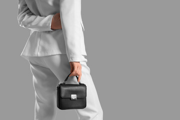 Young woman holding stylish black bag on grey background