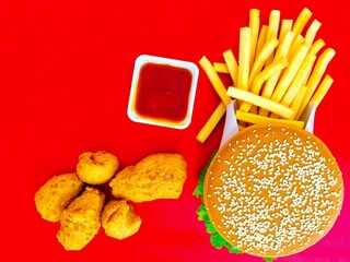 Delicious burger fries and chicken nuggets with ketchup on red background