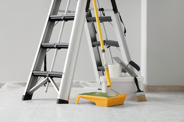 Metal stepladder with painter's tools near light wall in room