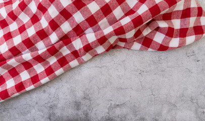 A red and white checkered tablecloth placed haphazardly and tilted on a cement surface