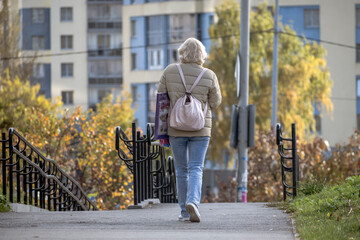 A woman with a backpack walks along the sidewalk on an autumn day