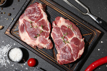 Wooden board with fresh raw steaks and cherry tomato on black background
