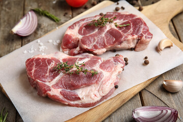 Cutting board with fresh raw steaks and different spices on wooden background, closeup