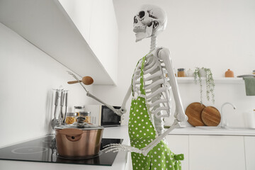 Human skeleton model with spoon and cooking pot on stove in kitchen