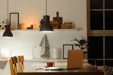 Fototapeta premium Laptop with coffee cup on table in kitchen at night