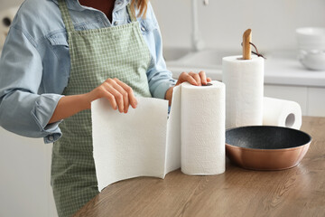 Young woman with rolls of paper towels and frying pan near table in kitchen, closeup