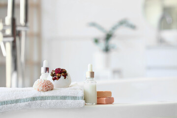 Bottles of cosmetic products, bath bombs, towel and soap bars on bathtub in interior of bathroom, closeup