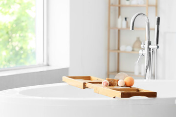 Wooden bathtub tray with bath bombs and soap bars in interior of bathroom, closeup