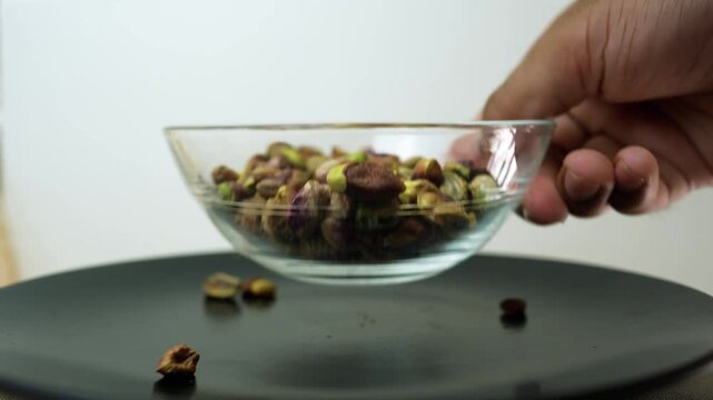 Hand holding a glass bowl of pistachios over a black surface
