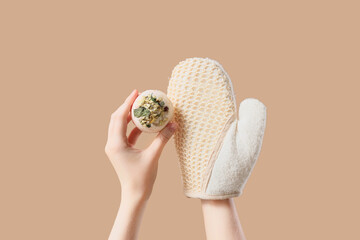 Female hands with bath bomb and massage glove on beige background, closeup