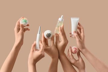 Female hands holding bath bombs and bottles of cosmetic products on beige background, closeup