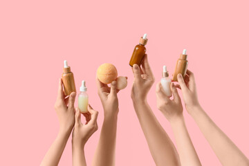 Female hands holding bath bombs and bottles of cosmetic products on pink background