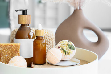 Tray with bath bombs, soap bar and bottles of cosmetic products on table in bathroom, closeup
