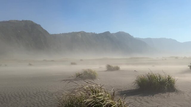 4k footage of mountain savannah with a strong wind gust creating a sand storm. Wind blows fast on the sea of sand, a volcanic sand storm. Located at the Mount Bromo caldera. Beauty of nature.