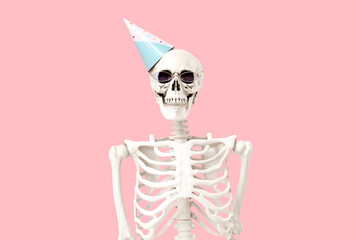 Human skeleton in party hat and sunglasses on pink background, closeup