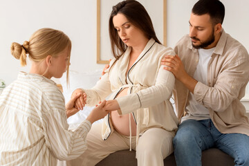 Obraz premium Young pregnant woman breathing with her husband and doula on bench near bed in bedroom
