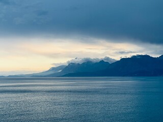 dark blue storm clouds, illuminated by the sun and merging with the dark sea and dark mountains