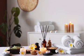 Plumeria flowers, clean towels, burning candles and bowls with sea salt on white couch in interior of spa salon