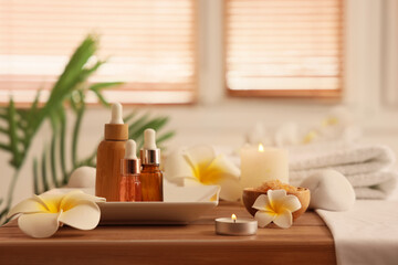 Tray with bottles of cosmetic products and plumeria flowers on table in interior of spa salon, closeup