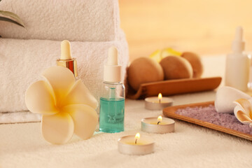 Plumeria flower, bottles of cosmetic products and burning candles on white couch in spa salon, closeup